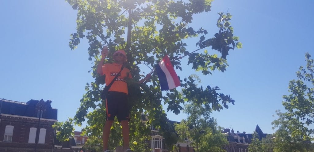 A lone Dutch supporter dressed in orange stands by a tree holding a Dutch flag for the 2019 FIFA Womens World Cup.