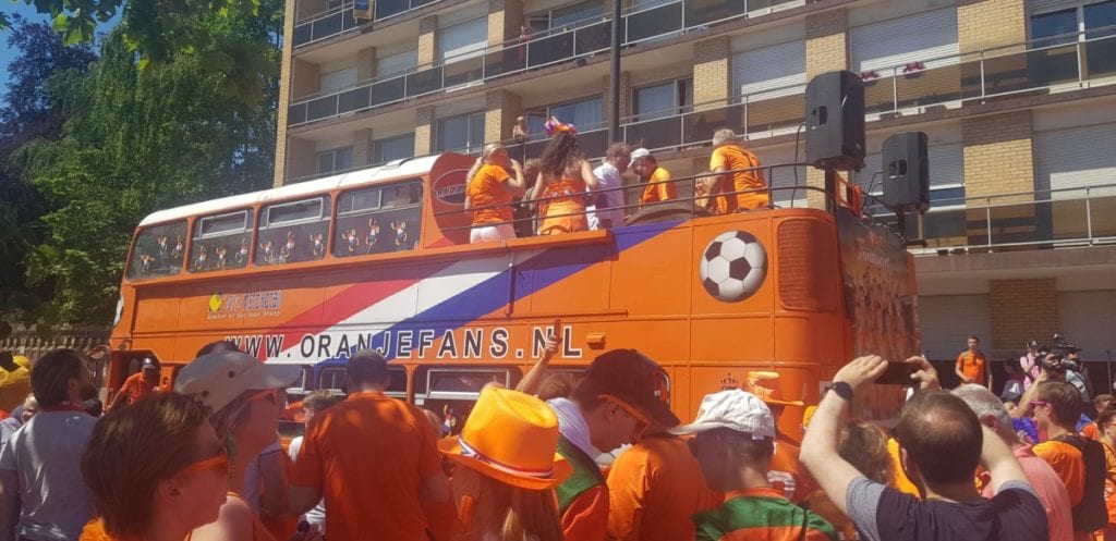 An orange double-decker bus is surrounded by Dutch fans at the 2019 FIFA Womens World Cup.