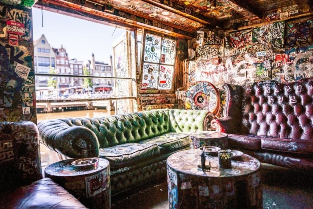 Colourful-couches-in-front-of-window-with-canal-view-an-graffiti-on-the-walls-at-smokers-bar-cafe-hill-street-blues-Amsterdam