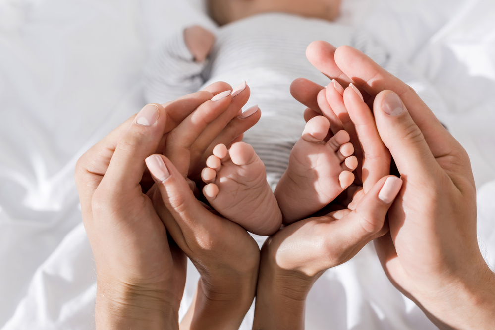 father-and-mother-hands-cupping-feet-of-newborn-baby