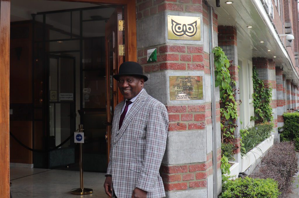 photo-of-doorman-at-boerejongens-west-coffeeshop-in-amsterdam-in-checkered-jacket-and-bowler-hat-smiling-at-camera