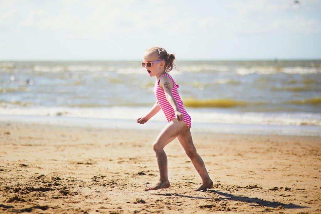Preschooler girl having fun on the sand beach at sea coast in Noordwijk, one of the best beaches in the Netherlands.