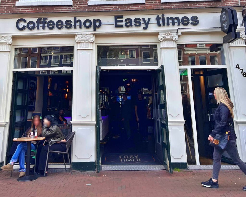 photo-of-exterior-of-easy-times-coffeeshop-with-two-girls-sitting-at-table-outside-and-blonde-woman-walking-past