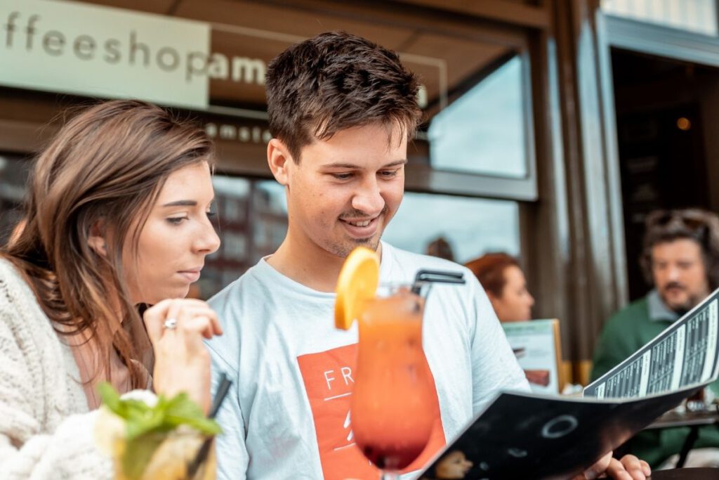 Young-couple-chosing-from-menu-at-coffeeshop-amsterdam-with-cocktails-on-the-table