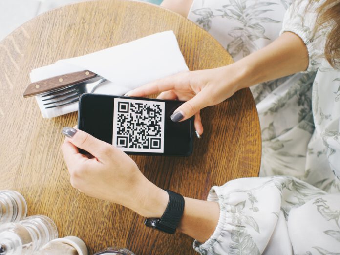 Woman-holds-smartphone-with-coronavirus-QR-code-in-cafe