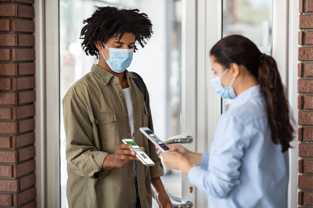 Woman-scans-corona-pass-of-a-young-man-both-wearing-masks
