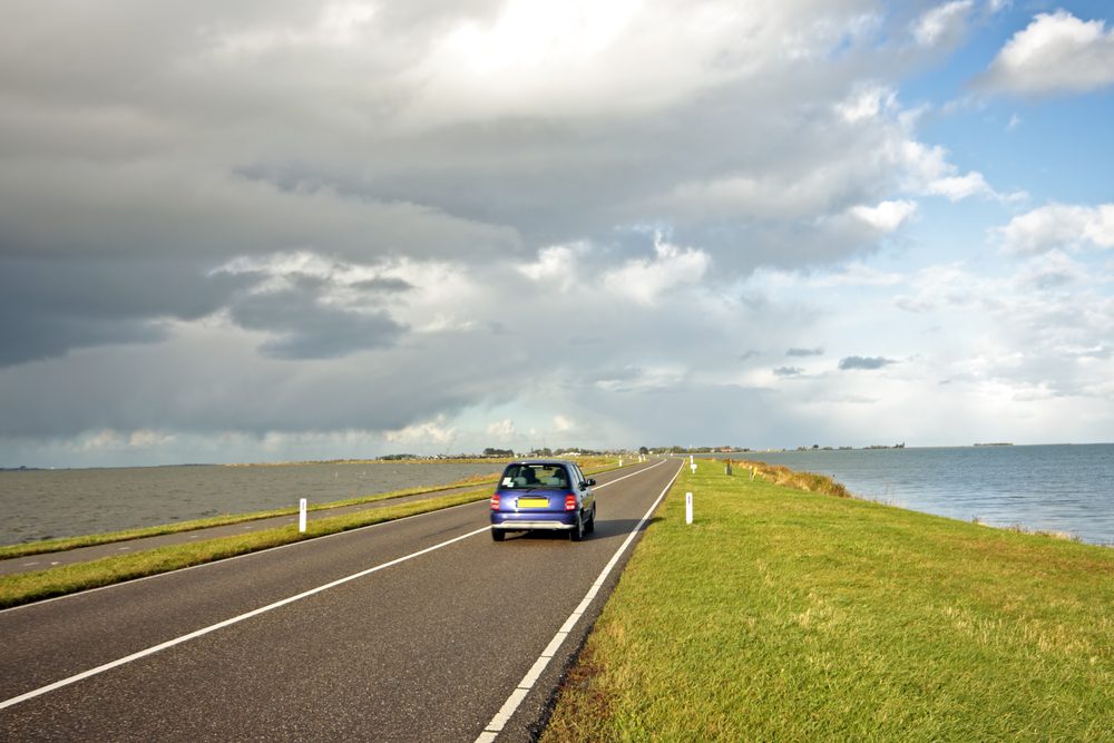 A-blue-car-driving-on-dyke-along-coastline-in-the-Netherlands-under-grey-sky