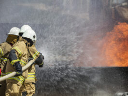 Three-fire-fighters-extingushing-fire-with-water-hose-in-beige-uniforms