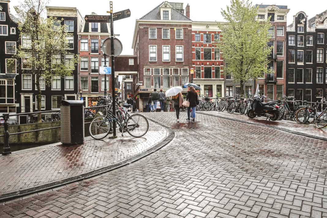 photo-of-rainy-weather-in-amsterdam-people-walk-over-a-canal-holding-umbrellas