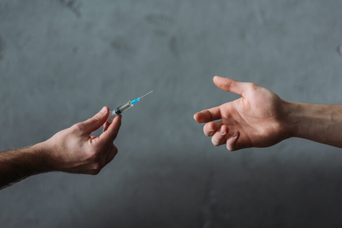 one-hand-offering-another-hand-a-syringe-with-heroin-against-grey-backdrop