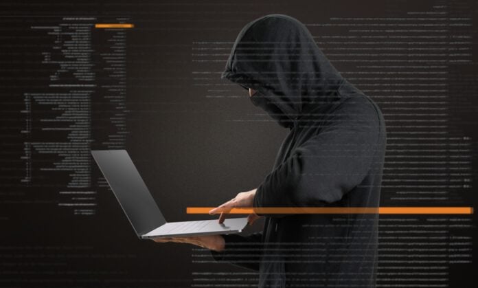 photo-of-man-wearing-black-hoodie-pulled-over-face-holding-laptop-standing-up-while-coding-appears-over-image