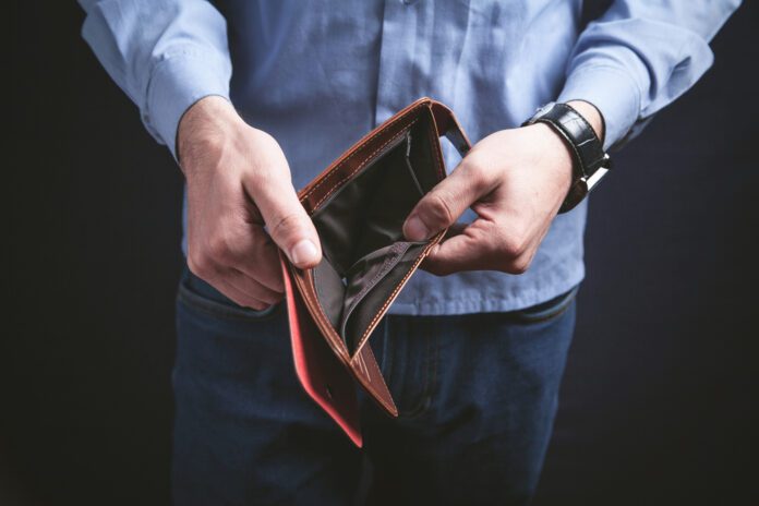 man-in-blue-shirt-and-jeans-holding-open-empty-wallet-against-black-background