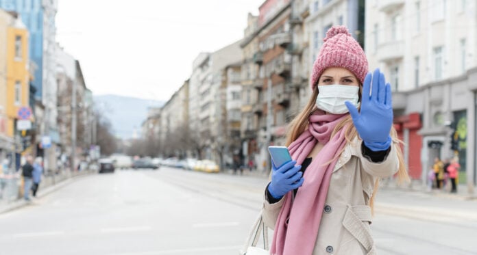 woman-with-mask-and-winter-hat-and-skarf-signalling-viewer-with-outstretched-hand-to-stay-away