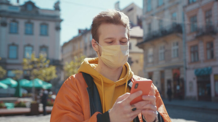 photo-dutch-young-man-with-facemask-looking-at-his-phone