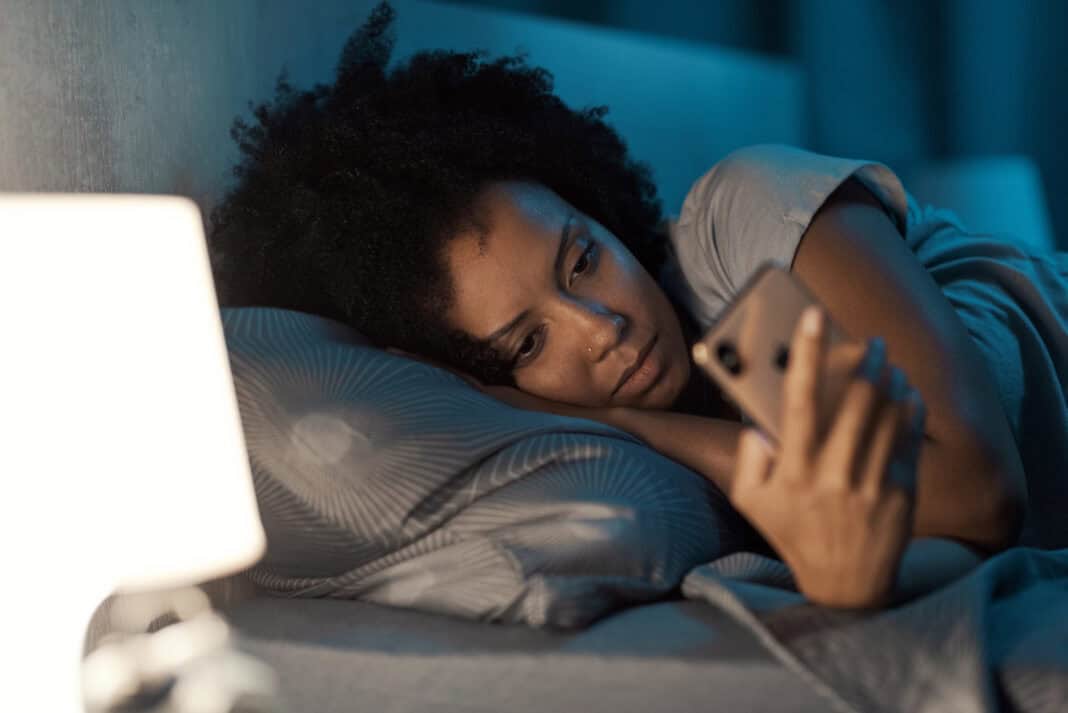 woman-laying-in-bed-checking-messages-on-her-phone-feels-upset-that-nobody-has-texted