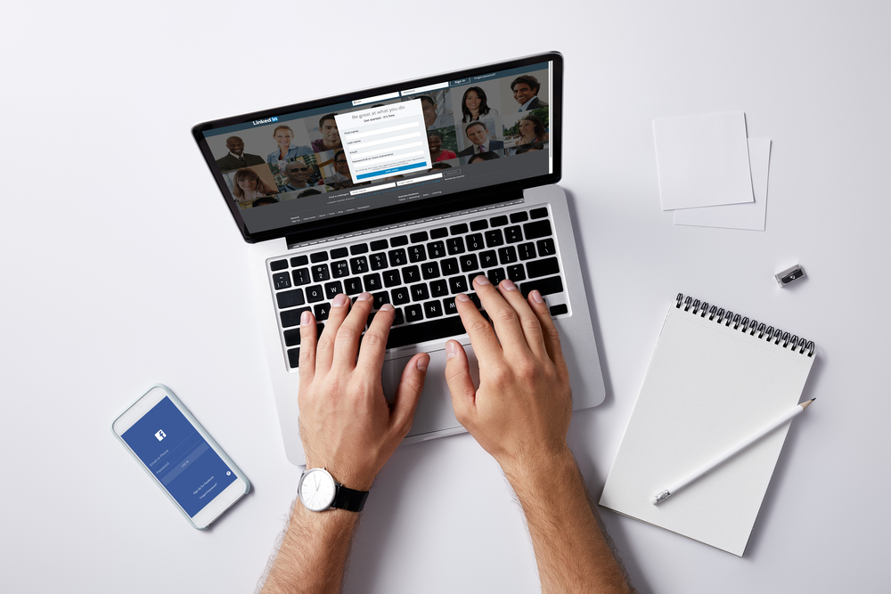 Man-using-LinkedIn-on-a-laptop-with-cellphone-and-notebook