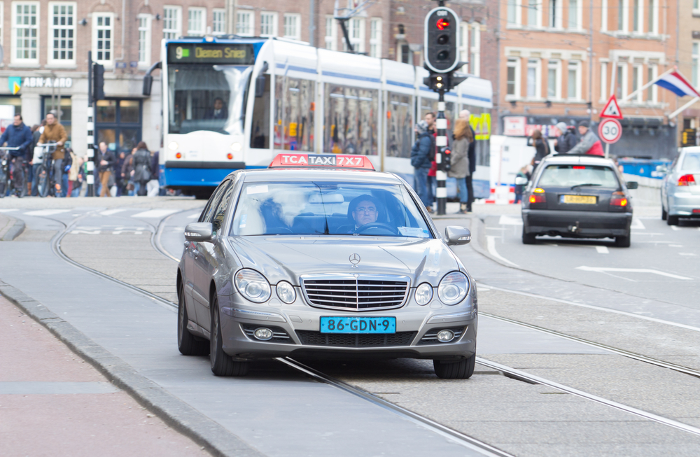 Taxi-driving-through-central-AMsterdam-in-front-of-a-tram