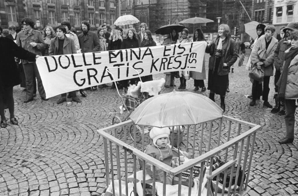 foto-de-bebê-sentando-em-um-cercadinho-público-no-protesto-dolle-minas-em-1971-com-placa-e-manifestantes-no-fundo