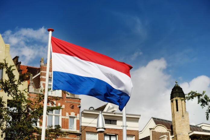 Dutch-flag-waving-in-blue-sky-in-front-of-buildings