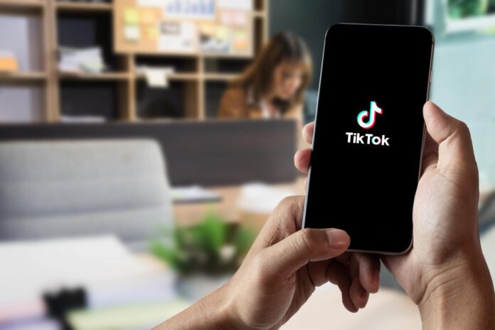 photo-of-person-using-TikTok-app-on-phone-while-in-office-with-woman-in-background