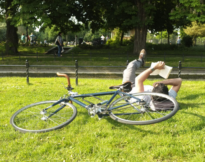 Dutch-man-laying-down-in-park-reading-near-bike-in-summer