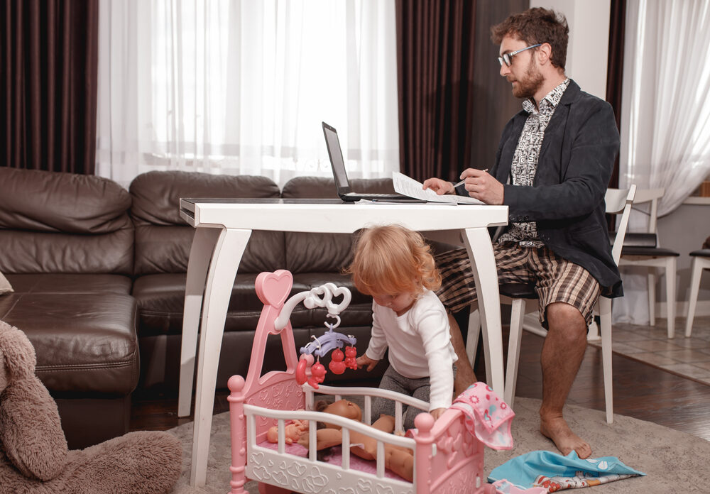 photo-of-man-working-from-home-in-his-underwear-while-taking-care-of-his-child-avoiding-the-office