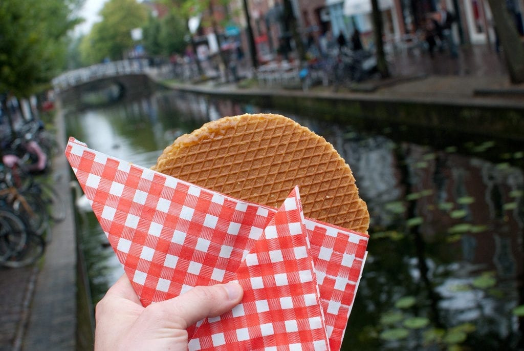 Stroopwafel held in front of a canal in Amsterdam