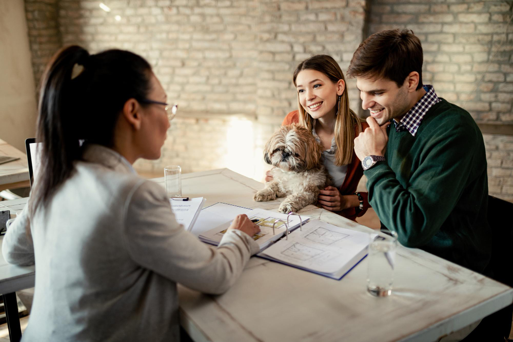 Photo-of-bidding-expert-speaking-with-couple-and-their-dog-at-table