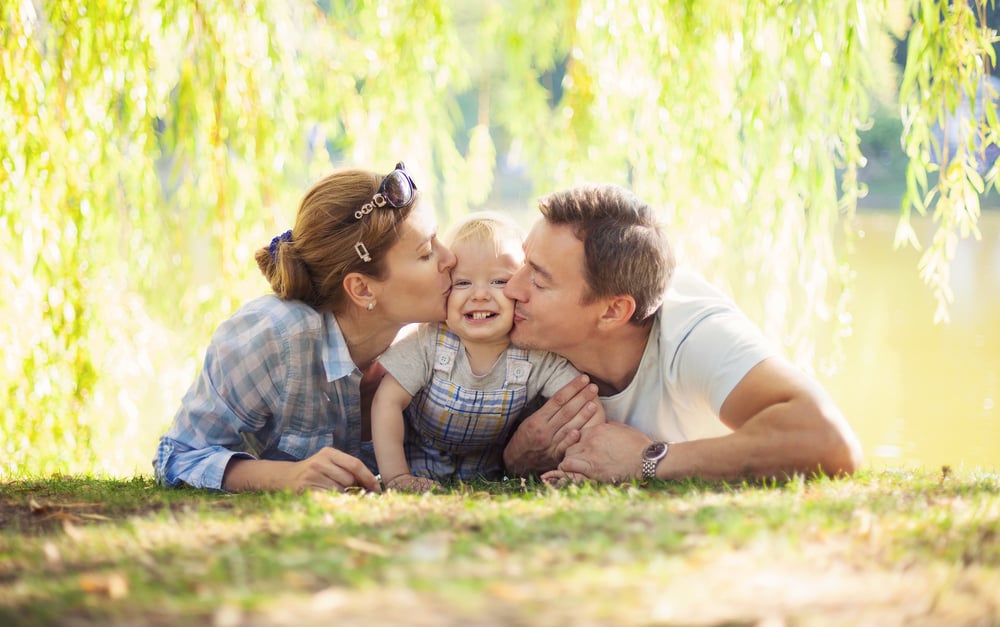photo-of-parents-kissing-smiling-baby-boy-on-cheek-both-cheeks-in-a-park