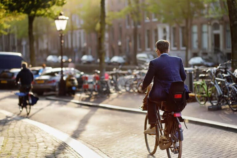 An elegantly dressed man rides a Bicycle in the center to go to his job in Amsterdam.