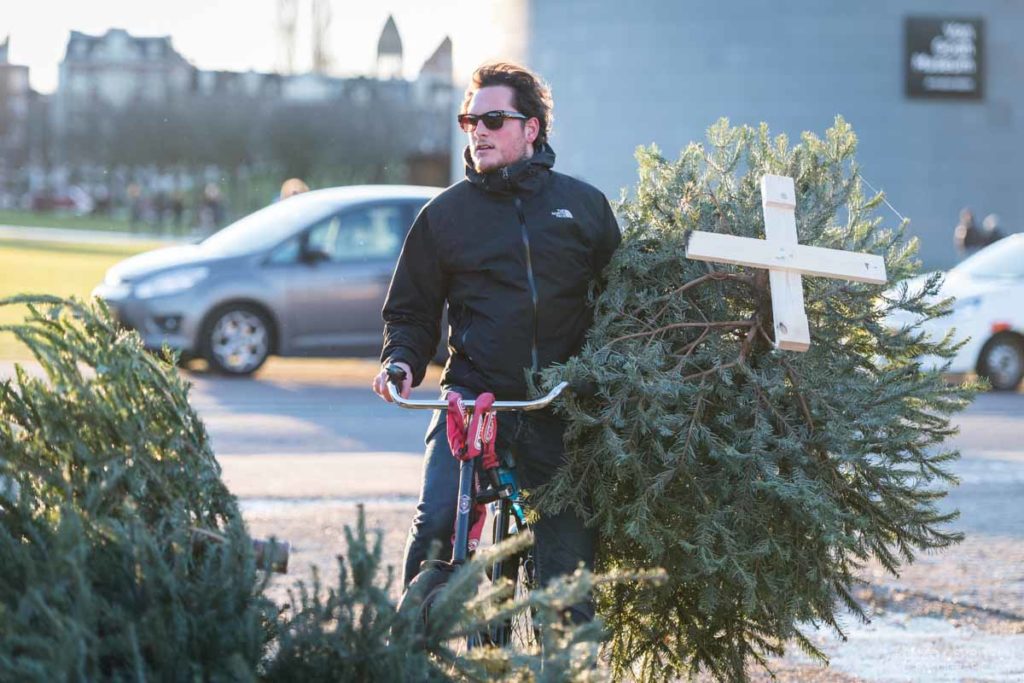 photo-of-man-holding-christmas-tree-waiting-to-drop-off-on-bike