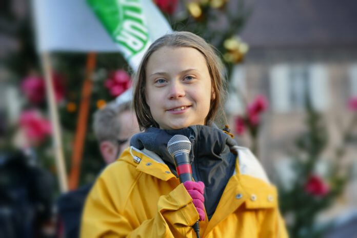 photo-of-greta-thunberg-at-protest-wearing-a-yellow-jacket-and-holding-a-mic-giving-a-speech