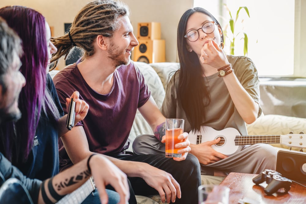 Group-of-friends-sitting-in-living-room-one-girl-with-black-hair-smoking-joint