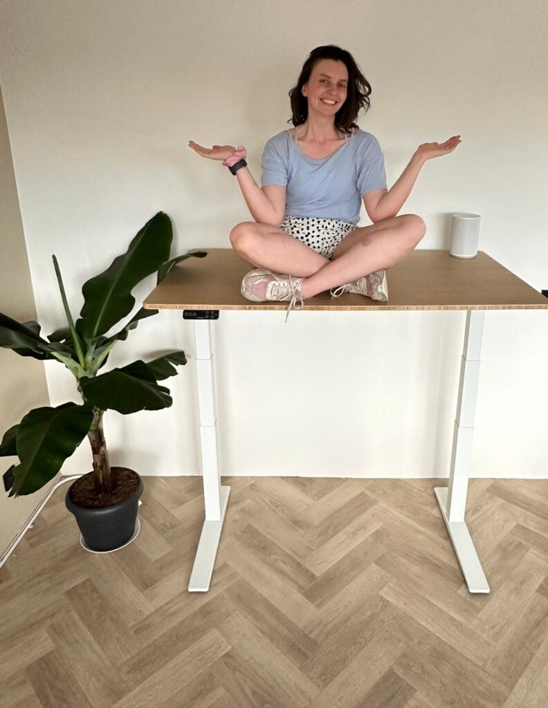 photo-of-woman-sitting-crosslegged-on-standing-desk-at-full-height-next-to-banana-plant