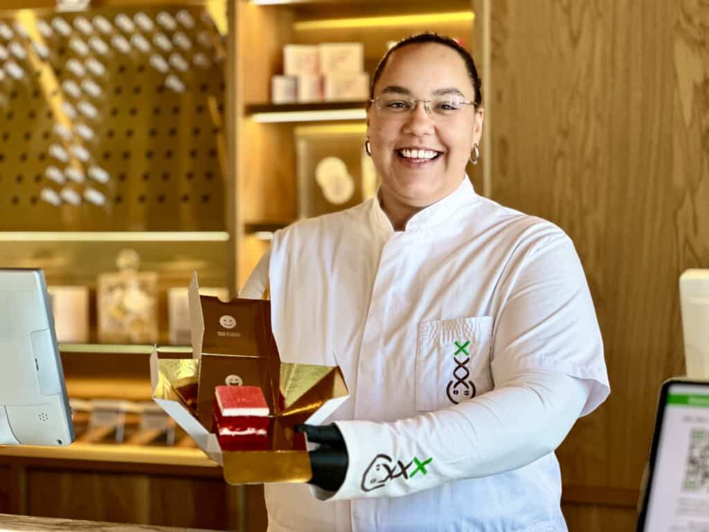 photo-of-smiling-budtender-looking-at-camera-holding-red-velvet-cake-edible-with-gold-coffeeshop-decor-behind