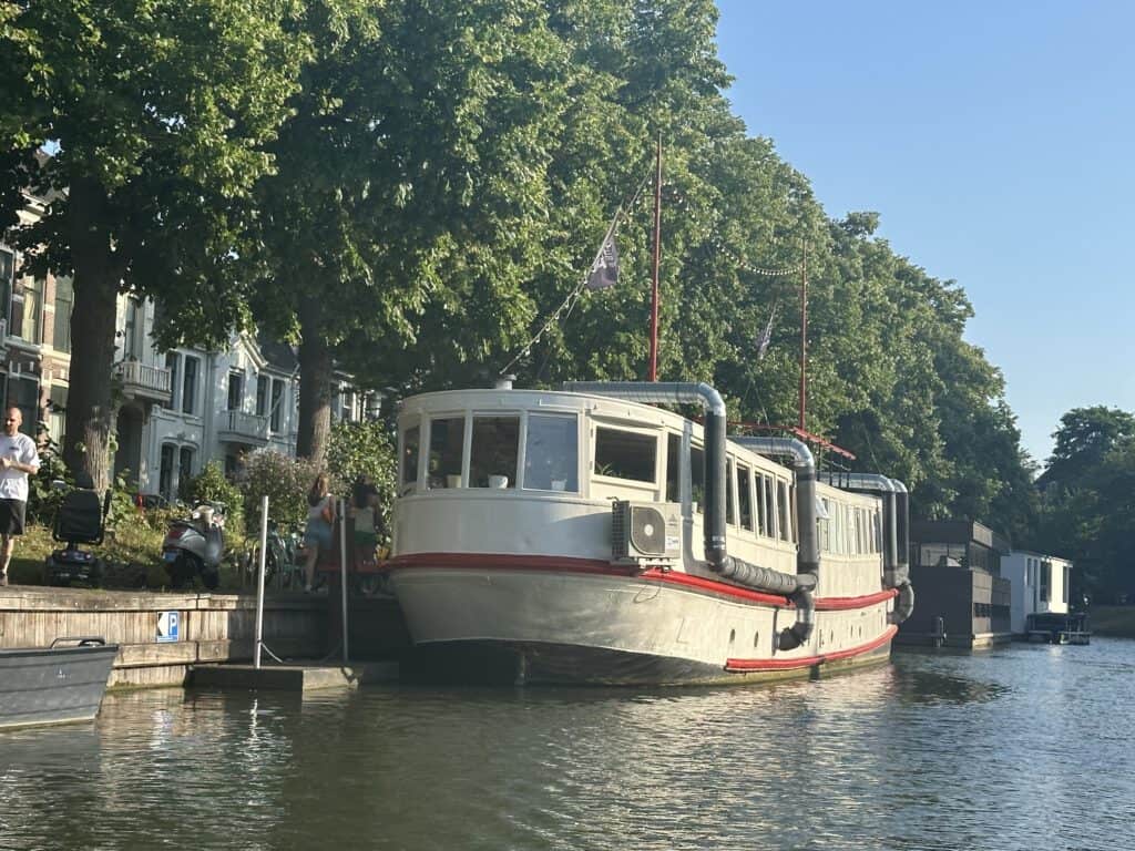photo-of-old-style-boat-culture-boat-coffeeshop-in-utrecht-floating-on-water-with-green-trees-behind