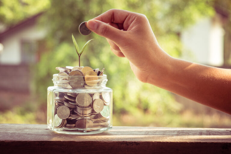 Photo-of-hand-putting-money-in-jar-with-leaves-sprouting