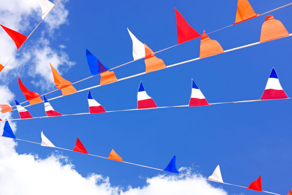 Red, white, blue, and orange flags hanging under a sunny, bright, blue sky