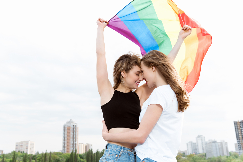 photo-of-two-woman-hugging-and-holding-up-the-LGBTQ+-flag