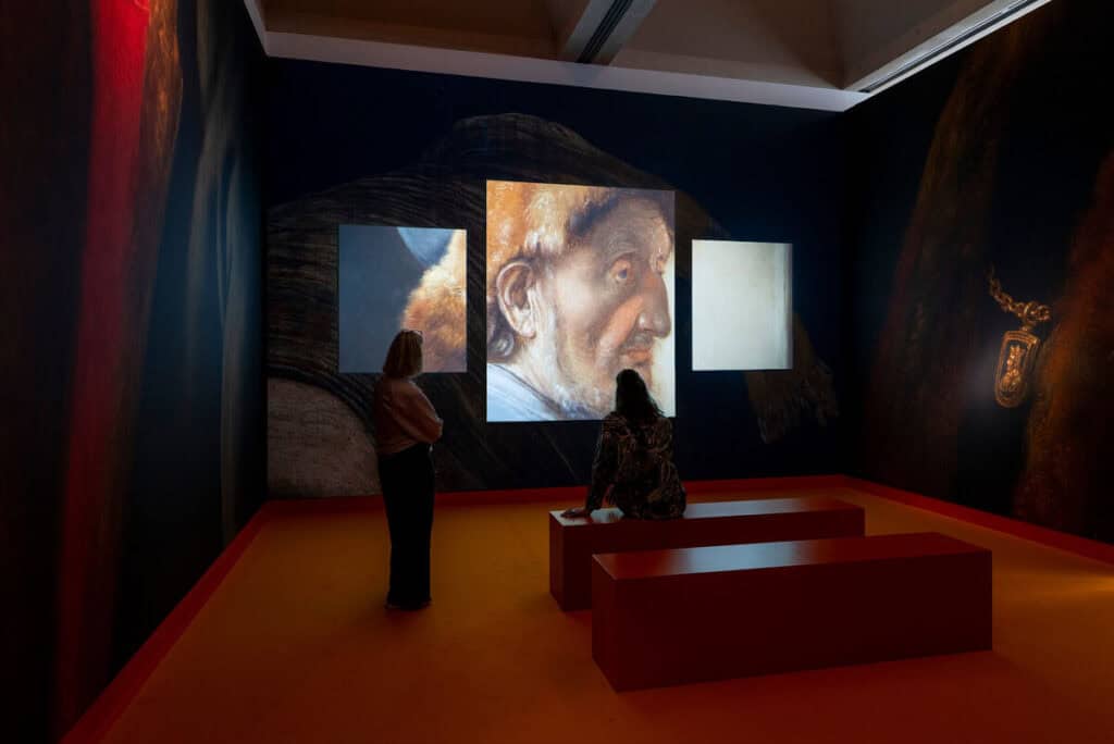photo-of-exhibition-in-the-lakenhal-museum-in-Leiden-showing-women-sitting-and-standing-in-dark-room-with-projection-of-painting-on-wall