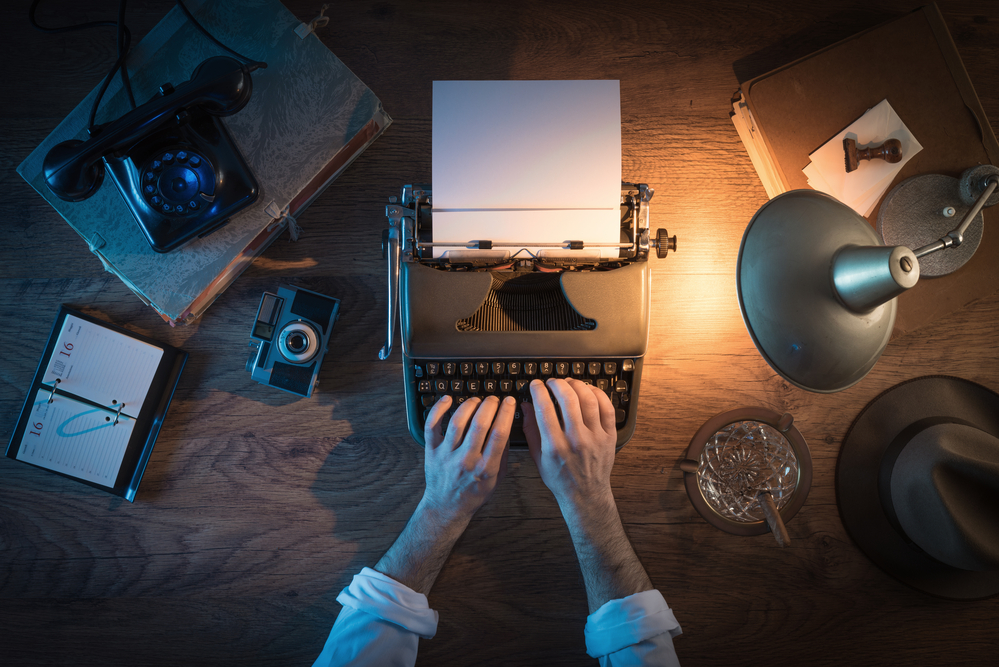 photo-of-desk-from-above-with-man-typing-at-type-writer-and-lamp-illuminating-the-scene