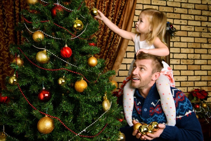 Dutch-man-carries-little-blond-daughter-on-shoulders-while-decorating-artificial-Christmas-tree-at-home-in-November