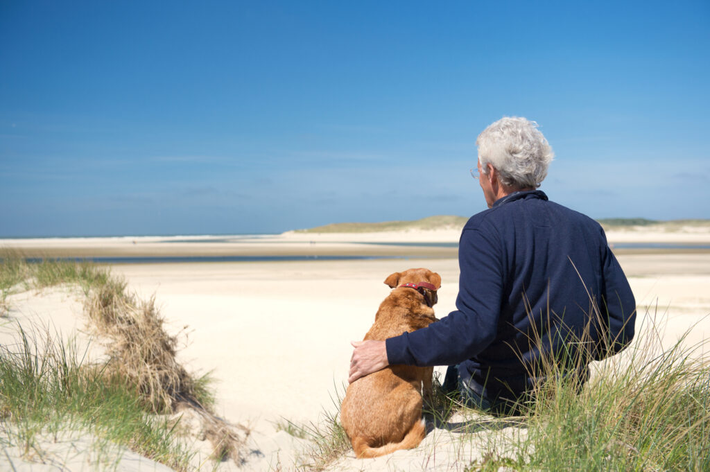 Man-sitting-with-his-dog-at-the-beach-in-texel