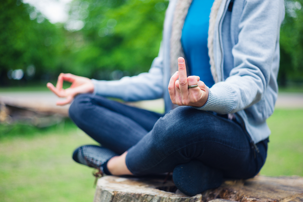 woman-sitting-cross-legged-in-meditation-with-ironic-middle-finger-hand-gesture