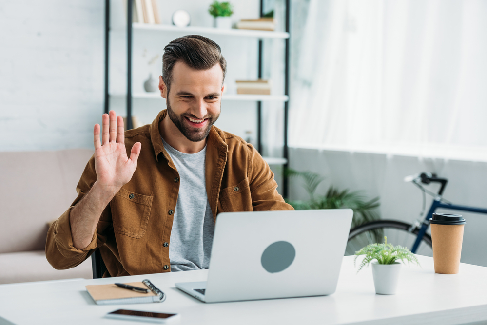 Photo-of-man-waving-at-laptop-during-online-meeting-from-home