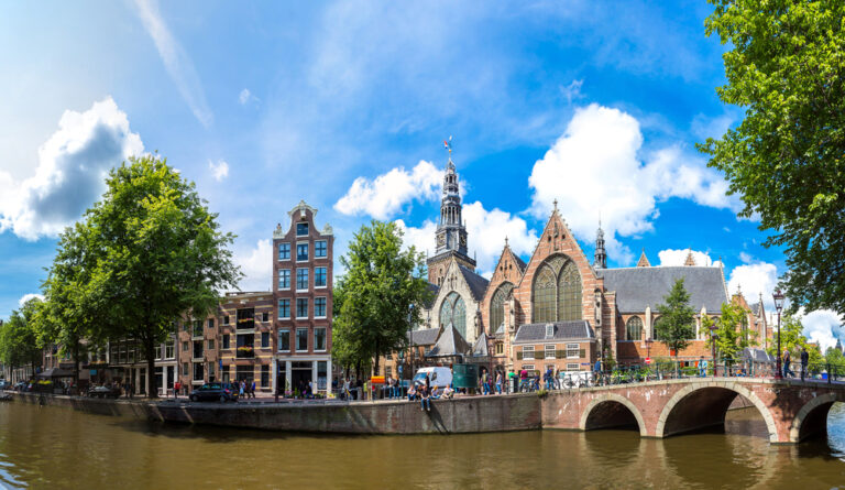 panorama-shot-of-the-old-church-in-Amsterdam-acros-a-Dutch-canal-under-blue-sky