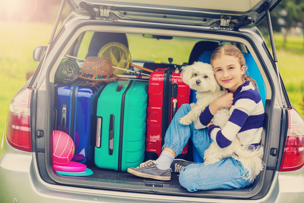 Young-girl-and-her-dog-sitting-in-car-trunk-with-luggage