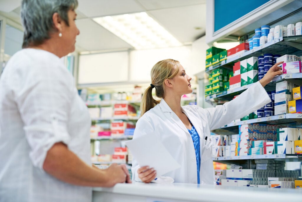 photo-of-pharmacist-in-the-Netherlands-helping-customer-looking-at-prescriptions-on-shelf-in-Dutch-pharmacy