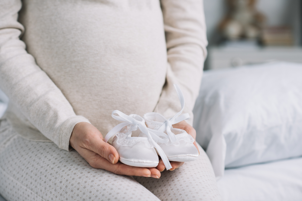 Pregnant-woman-dressed-in-beige-sweter-and-pants-holding-pair-of-baby-shoes-in-cupped-hands