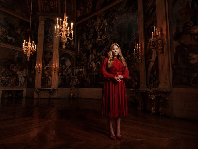 Landscape-picture-of-crown-princess-amalia-of-the-netherlands-in-a-red-dress-and-dark-room